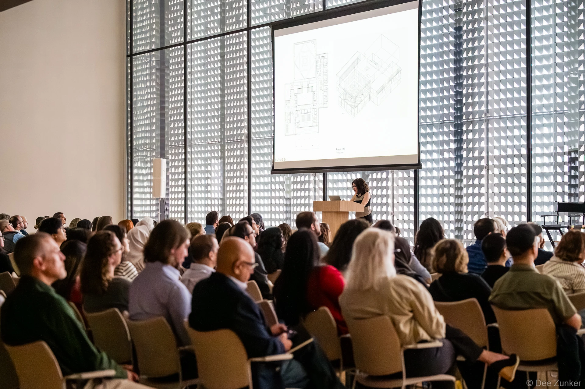Audience attending Gulf Coast Green 2026 keynote at The Ismaili Center Houston, with architectural floor plan projected on screen behind podium speaker.