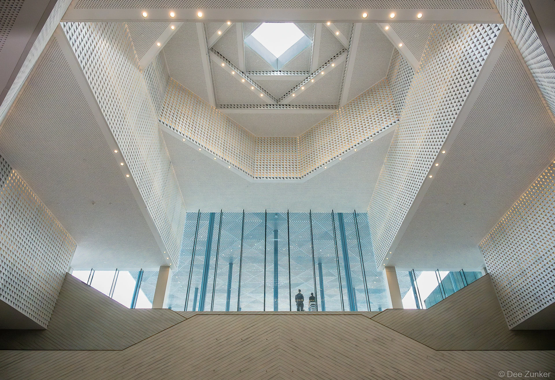 Looking up into the geometric faceted atrium ceiling of the Ismaili Center Houston, with two attendees visible on a mezzanine balcony during Gulf Coast Green 2026.