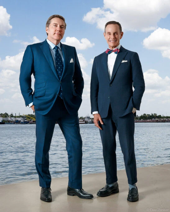 Two male attorneys in navy suits pose outdoors near a Houston waterway in a professional environmental portrait by Dee Zunker Photography.
