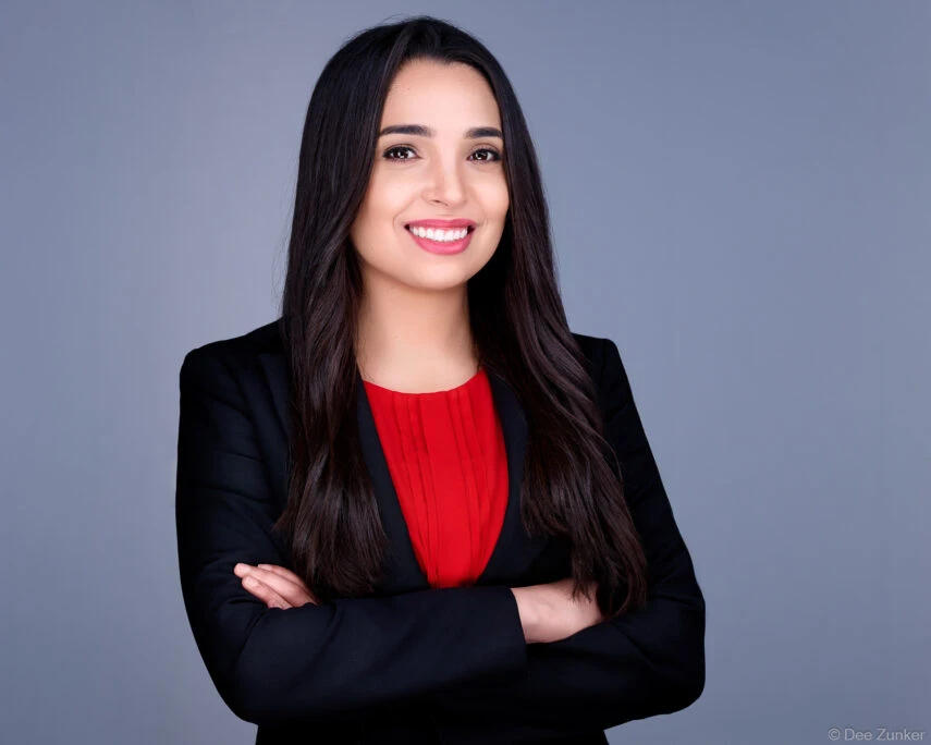 Professional corporate headshot of a woman in black blazer and red top, arms crossed, smiling, studio gray background, Houston.