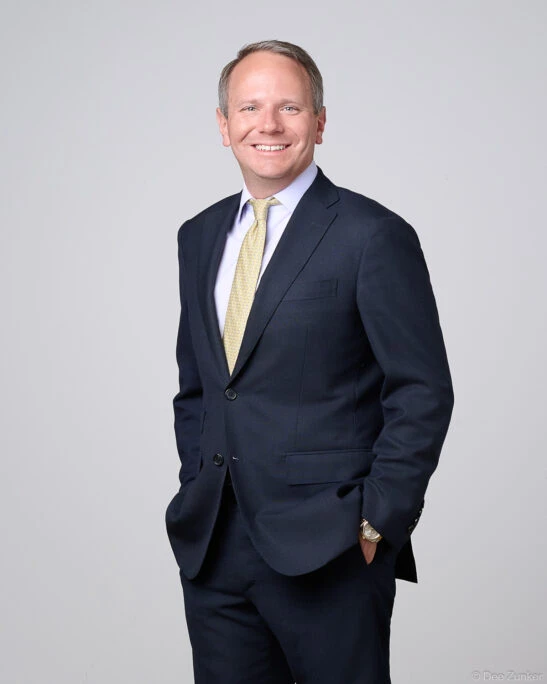 Male financial executive in navy suit and gold tie poses for a corporate studio headshot in Houston, gray background.