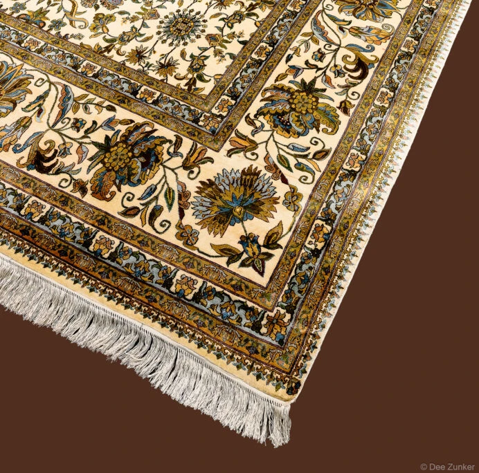 Close-up product photo of an antique silk oriental rug with ivory field, floral motifs, gold border, and cream fringe.
