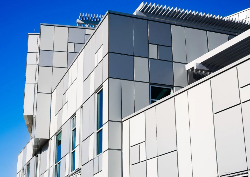 Upward view of a modern Houston commercial building exterior featuring white and dark gray metal cladding panels against a vivid blue sky.