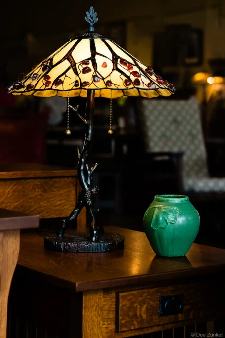 Tiffany-style stained glass lamp with branch base beside a green ceramic vase on a Mission oak side table, Houston product photography.