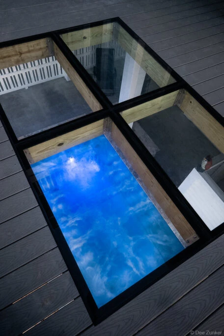 Glass flooring panels set into a gray composite residential deck, revealing a blue illuminated pool below, shot for product portfolio.