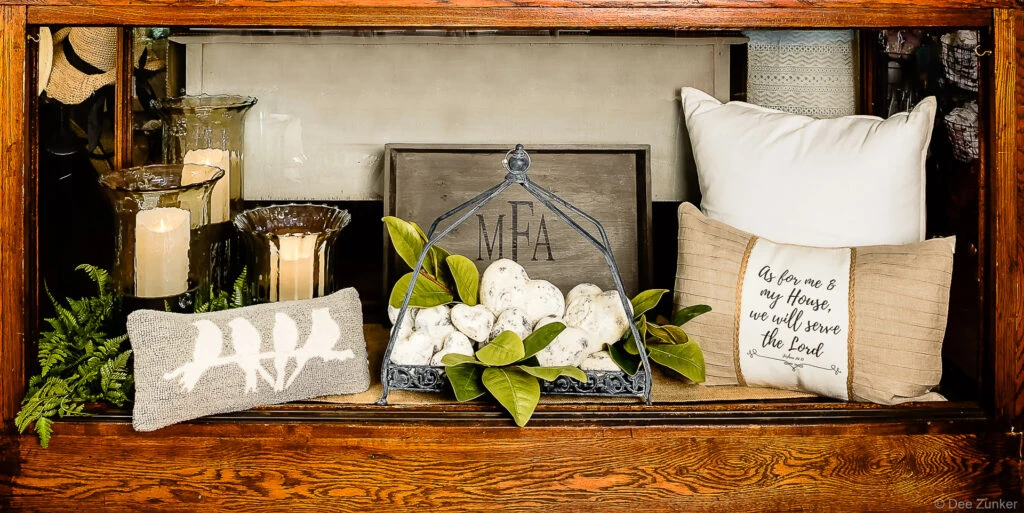 Styled retail vignette featuring decorative pillows, candles, magnolia leaves, and monogram sign photographed for Houston product portfolio.