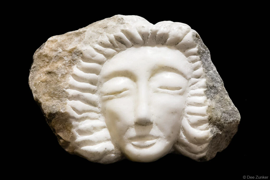Polished white marble face sculpture with radiating carved rays emerging from rough stone, Houston product photography by Dee Zunker.