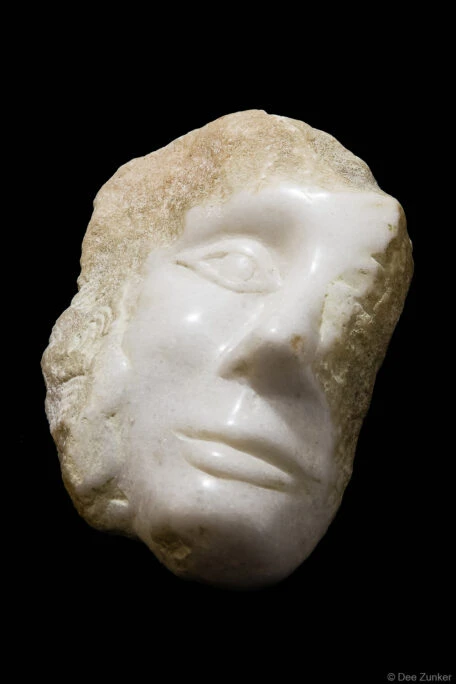 Close-up product photo of a white marble ancient face sculpture fragment against black background, Houston studio photography.