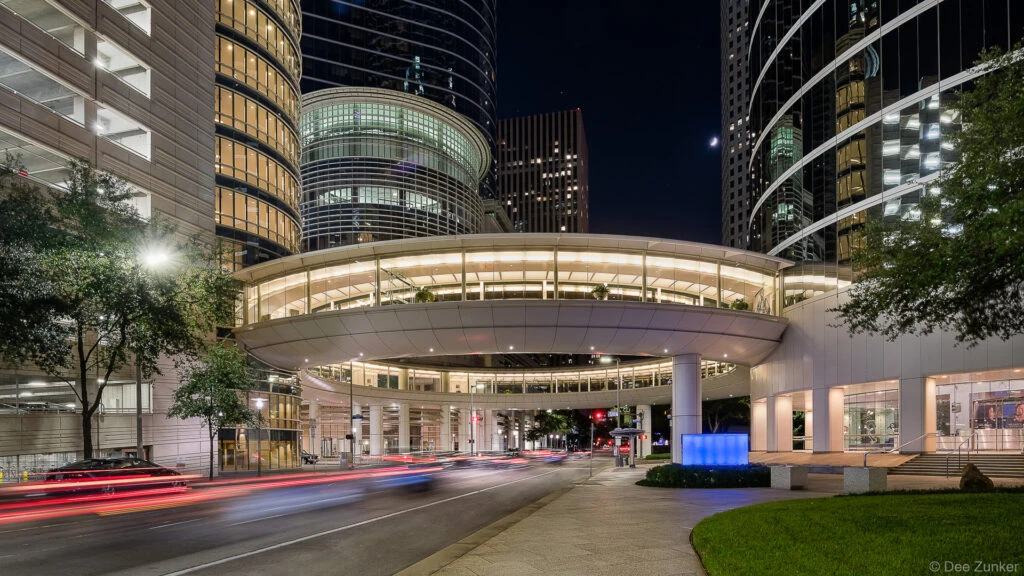 Nighttime exterior of a curved glass office tower at 1300 Smith Street Houston with light trails from passing traffic