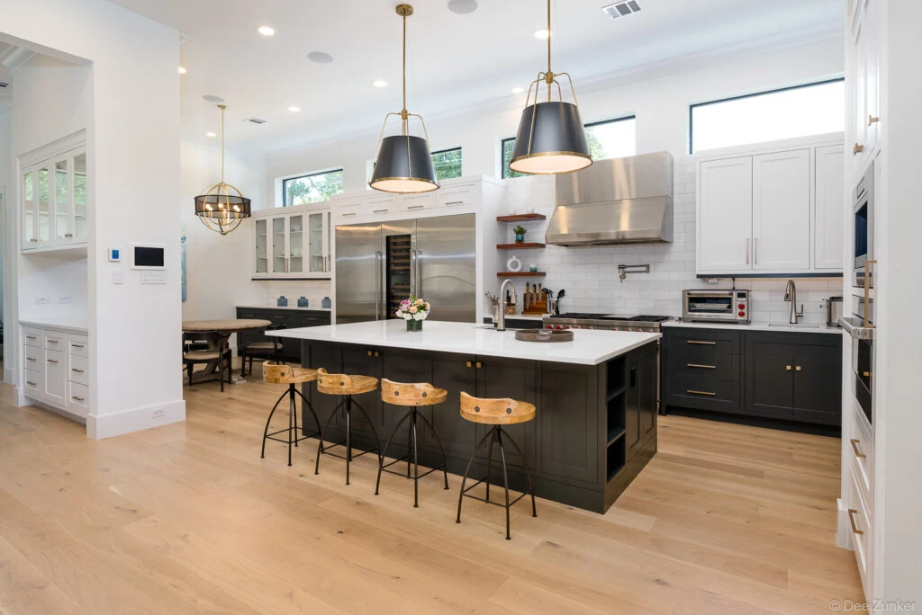 Luxury Houston kitchen with dark ebony cabinetry, white quartz island, brass pendant lights, and wood barstools over light hardwood floors.
