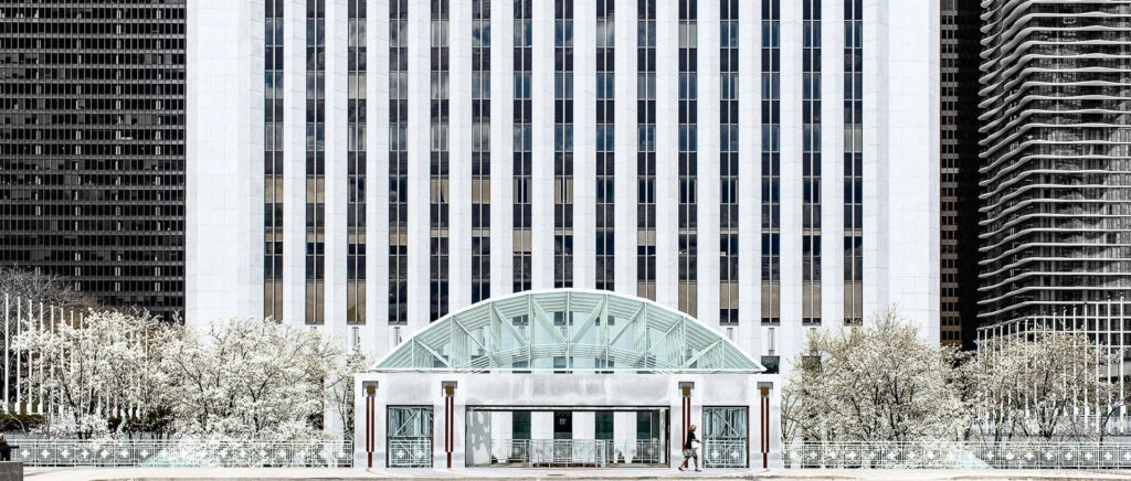 Exterior architectural photography of a large white office tower with glass canopy entrance and flowering trees in Chicago