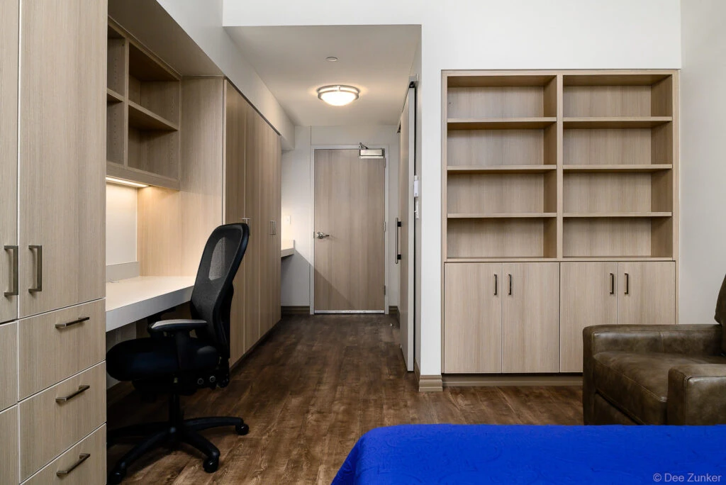Modern student housing bedroom with built-in desk, shelving, wardrobe, ergonomic chair, and blue bedding at Axis St Marys Houston.