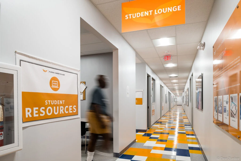 Bright college hallway in Southwest Houston featuring orange and blue tile flooring, student lounge signage, and student resources room entrance