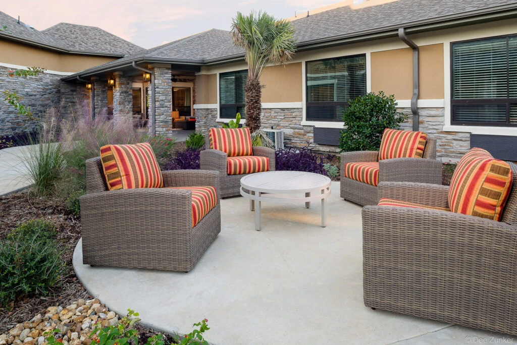 Wicker lounge chairs with striped cushions arranged around a white coffee table on a concrete patio at a College Station senior living facility.