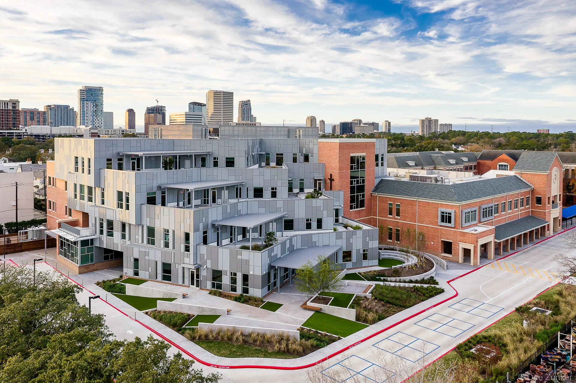 Aerial view of Cornerstone school campus with modern steel addition beside brick buildings, Houston skyline in background.