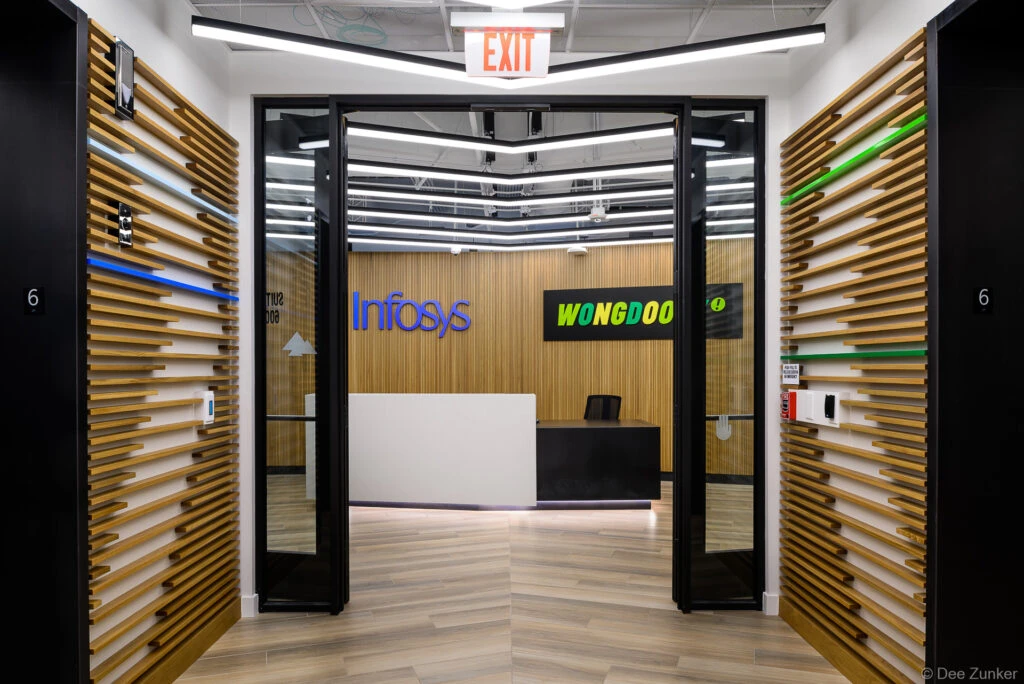 Modern corporate office entrance with wood slat walls, black glass doors, LED lighting, and a reception desk visible beyond the threshold