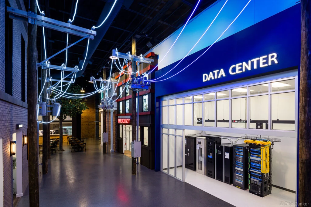 Interior architectural view of a corporate experience center Data Center exhibit with server racks, utility poles, and glowing cable displays in Houston.