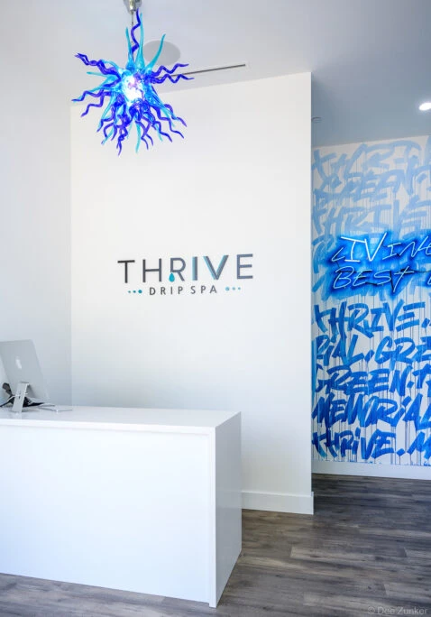 Modern white reception desk with blue art glass chandelier and graffiti-style mural wall inside a Houston drip spa at Memorial Green.
