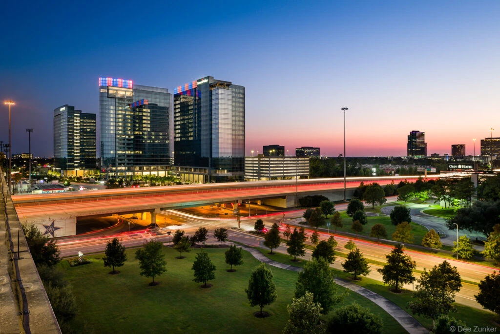 Aerial twilight view of Eldridge Parkway and I-10 interchange in Houston Energy Corridor with illuminated office towers and light trails