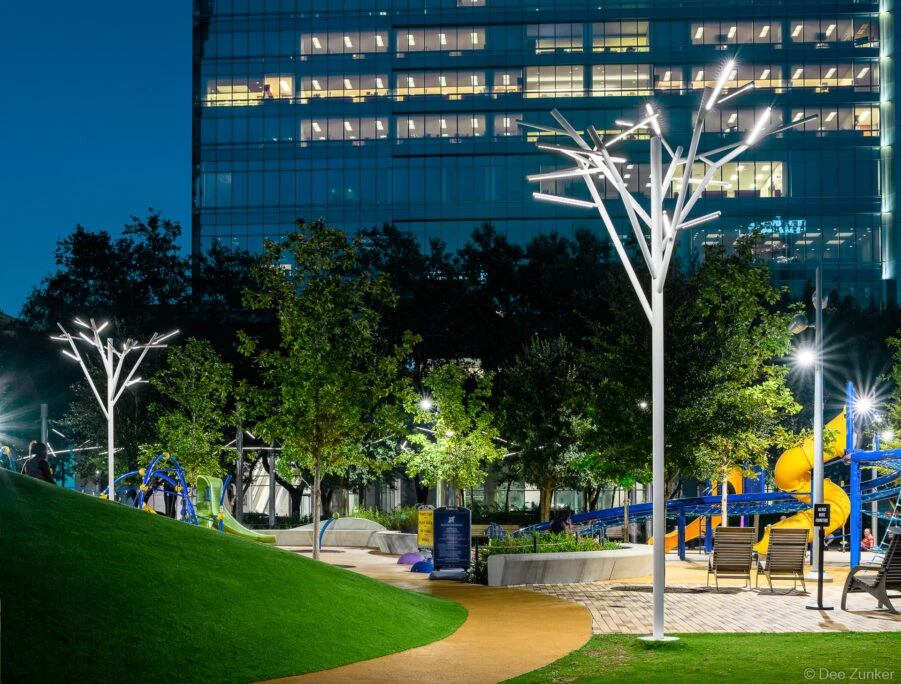 Tree-shaped LED light sculptures illuminating Discovery Green Park at night with colorful playground equipment and downtown Houston skyscraper backdrop
