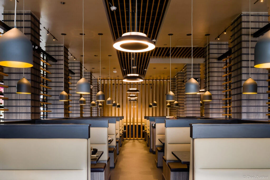 Symmetrical Japanese BBQ restaurant dining room with cream leather booths, pendant lights, and wood slat columns in Houston.