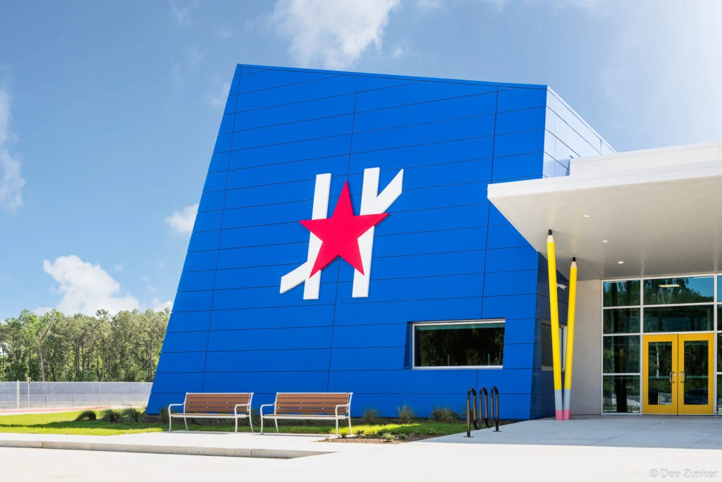 Exterior of a bold blue school building in Spring TX featuring oversized pencil sculptures and a red star logo near the entrance