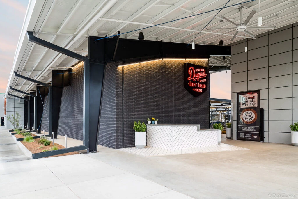 Exterior entrance of a baseball-themed entertainment venue in Katy TX featuring neon signage dark brick and a modern reception desk