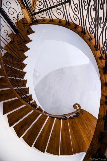 Aerial view of elegant spiral staircase with dark wood treads, ornate wrought iron railings, and marble flooring below in a Houston luxury residence.