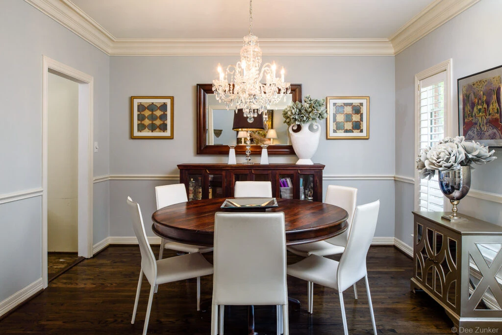 Elegant Houston dining room with crystal chandelier, round walnut table, white modern chairs, and classic crown molding interior design.