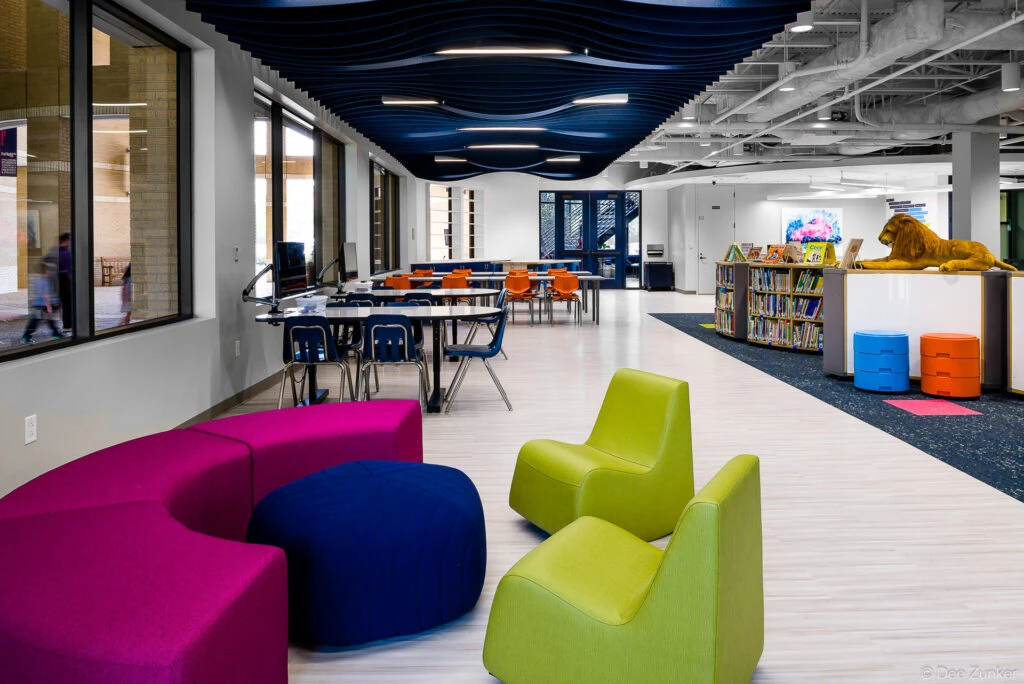 Colorful modern school library interior with modular seating, bookshelves, and a decorative wave ceiling installation in Houston