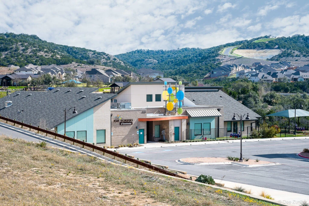 Exterior view of a modern preschool building in Austin TX with colorful circular sculpture accent and Texas Hill Country backdrop