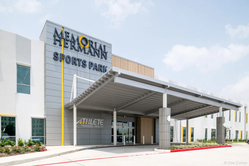 Exterior entrance of a modern Houston sports medicine and athlete training facility with covered canopy and bold signage