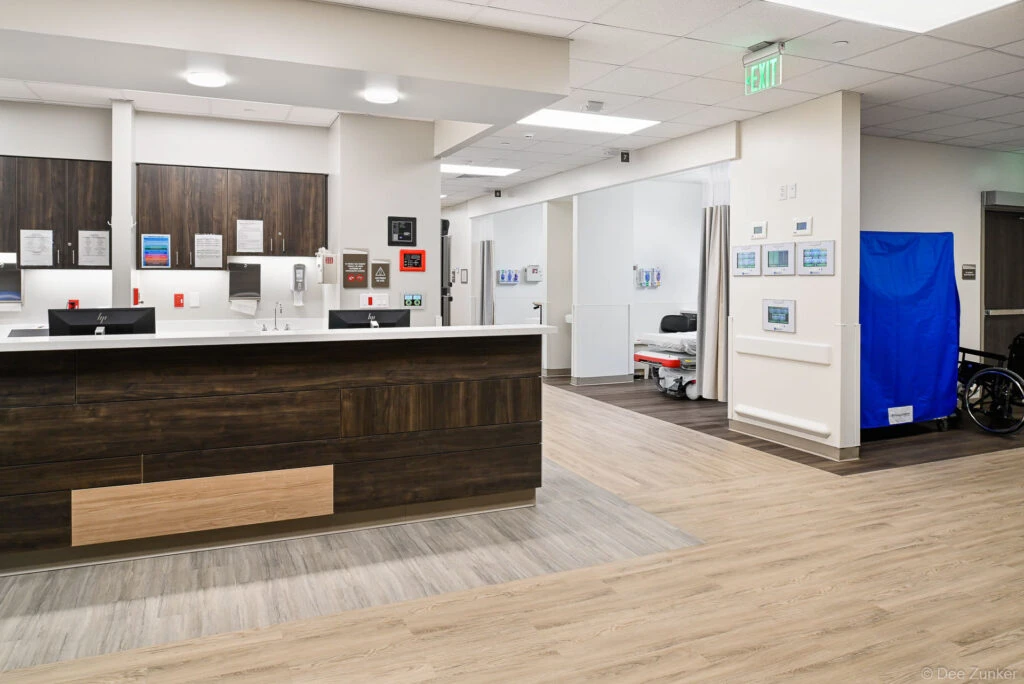 Newly renovated hospital nurses station with dark wood desk, HP monitors, privacy curtains, and wheelchair visible in Houston medical facility.