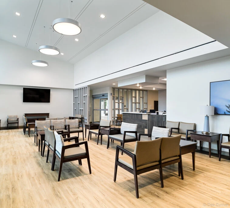 Spacious modern medical waiting room with wood-look floors, pendant lights, upholstered chairs, and reception desk in Houston facility.
