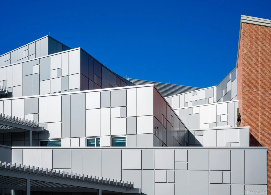 Contemporary commercial building exterior with geometric white metal panel cladding and dynamic roofline against clear blue sky, Houston TX.