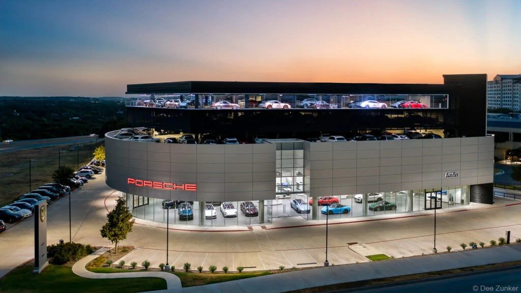 Aerial drone twilight view of a luxury automotive dealership exterior in Austin Texas with illuminated rooftop car display