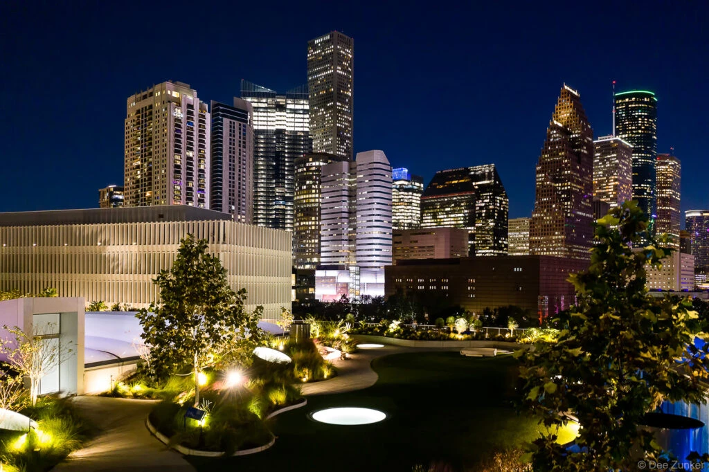 Walkable glass skylight floors on The Post Houston rooftop garden at twilight with illuminated downtown Houston skyline backdrop