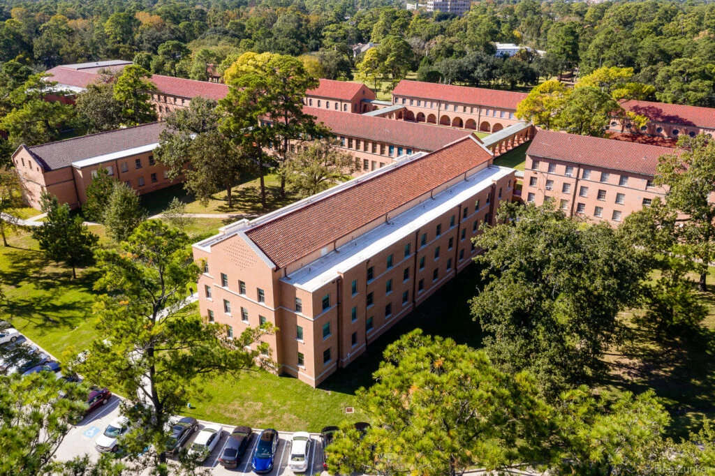 Aerial drone view of St. Mary's University campus buildings featuring red tile roofs, pink brick facades, and tree-lined grounds in Houston, TX.