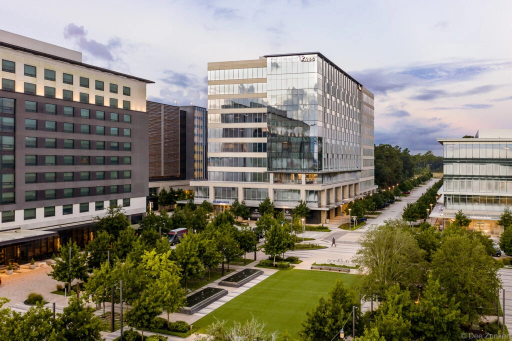 Aerial drone view of a modern glass office tower and courtyard with landscaped green space in The Woodlands, Texas at early morning