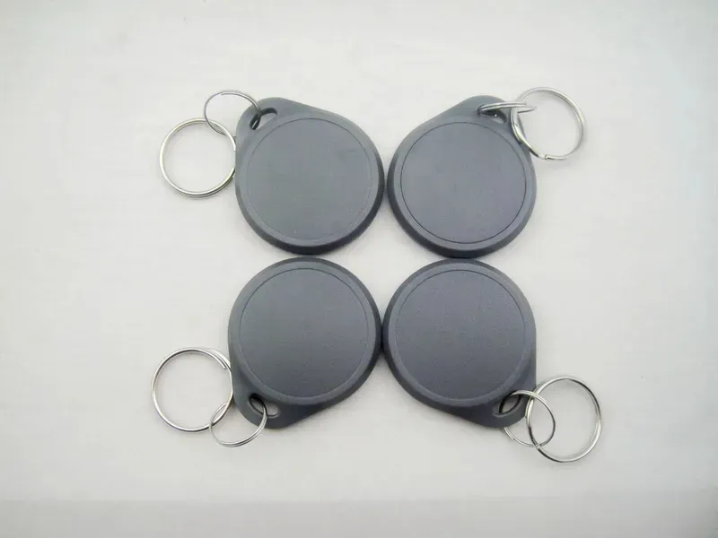 Fjouwer Dual Frequency Key Fobs mei metalen kaai ringen, elk yn griis, wurde organisearre yn in twa-by-twa raster op in wyt oerflak.