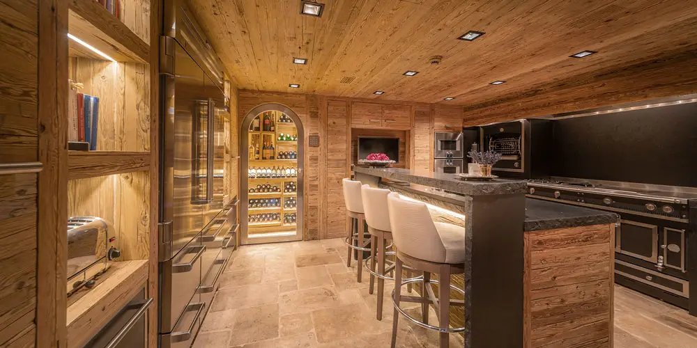 Luxury Verbier chalet kitchen & wine cellar at GuestLee, with wood accents, marble island, and glass wine wall for upscale rentals. | GuestLee luxury rental Switzerland