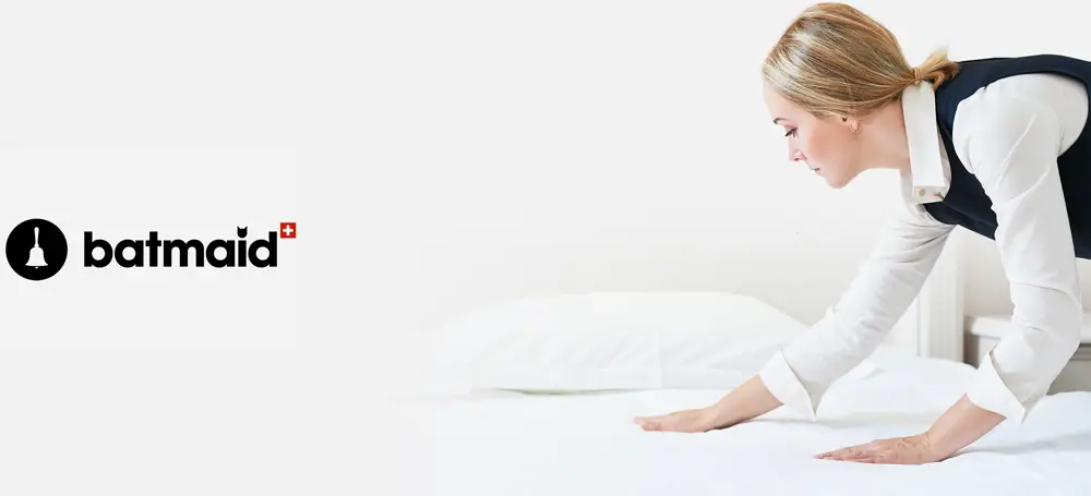 LEE_Ménage_Bat Housekeeper in uniform prepares a luxury bed with white linens for GuestLee’s premium Swiss rental in Verbier or Montreux. | GuestLee luxury rental Switzerland