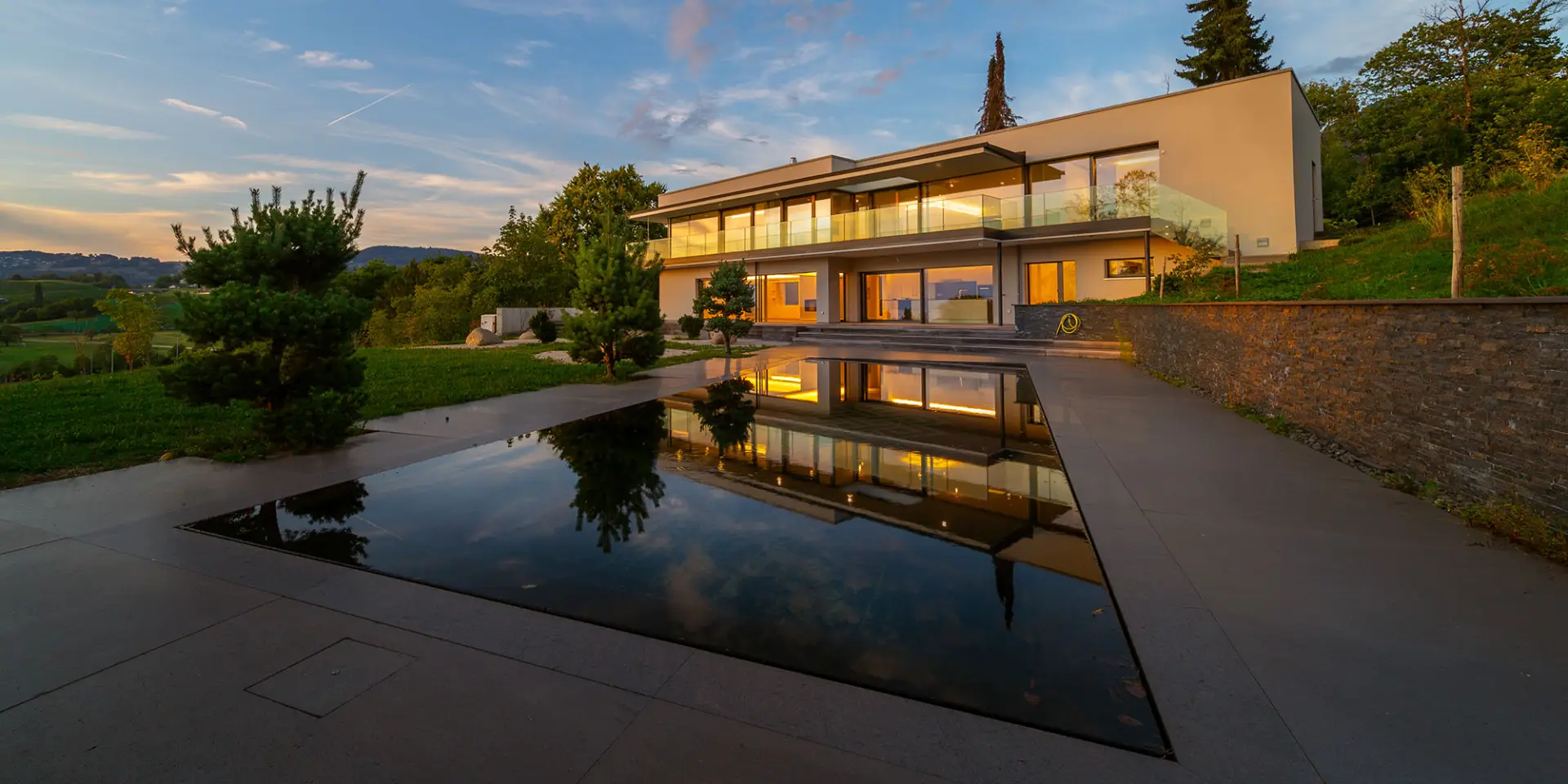 LEE_Owner_1 Luxury Geneva villa rental with floor-to-ceiling windows, elegant lighting, water feature, lush garden—GuestLee Switzerland. | GuestLee luxury rental Switzerland