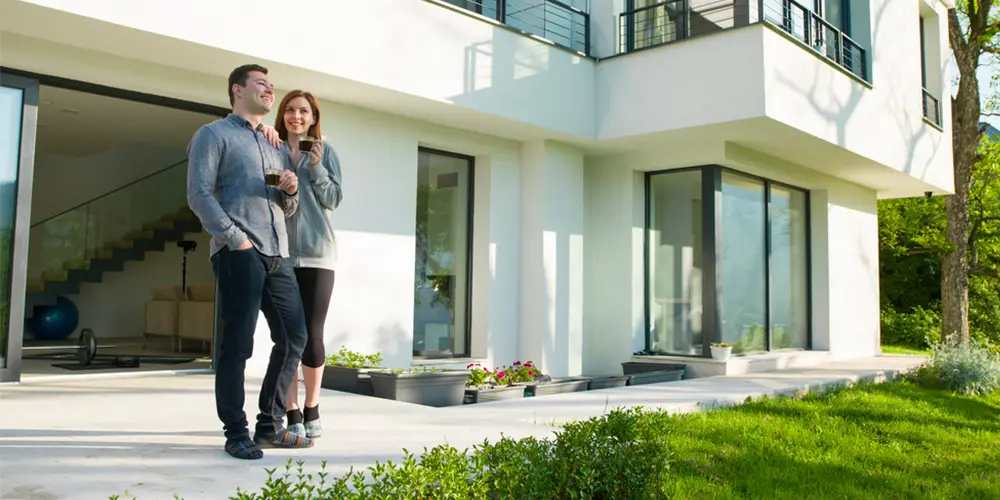 lee-1000-500-buyorsell Happy couple outside a luxury Geneva villa with large windows and lawn, enjoying sunny Swiss day at a GuestLee rental property. | GuestLee luxury rental Switzerland