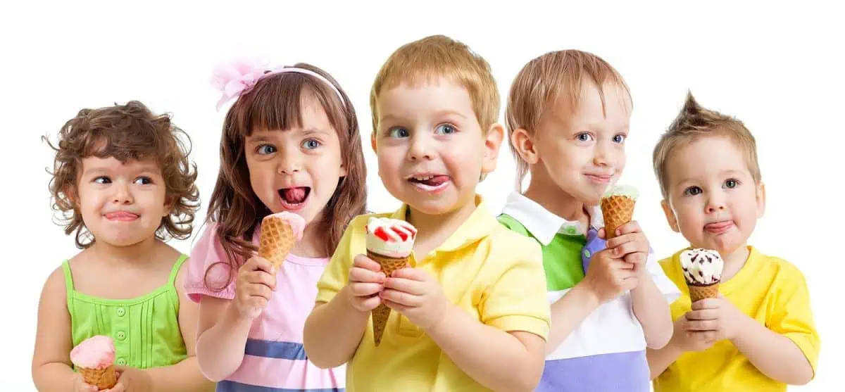 Five children stand in a row, each holding an ice cream cone. They are smiling and looking in different directions, like a playful child modeling shoot against a plain white background.