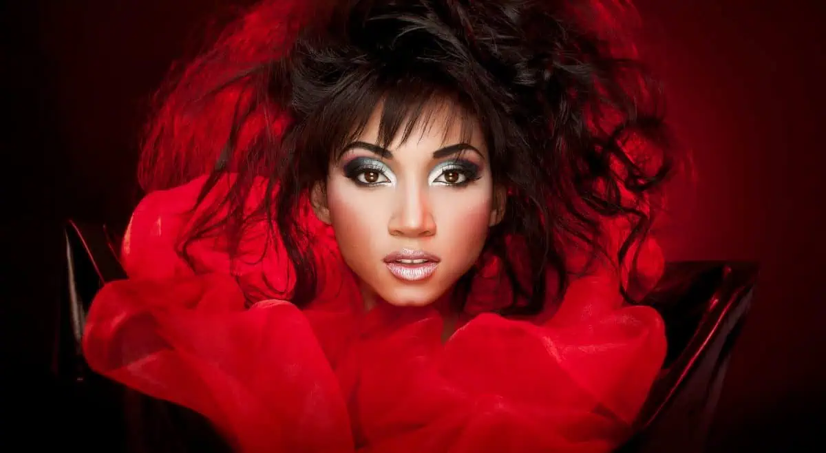 A person with dramatic makeup and styled dark hair is surrounded by red fabric, set against a striking red and black background, exquisitely illuminated by a beauty dish.
