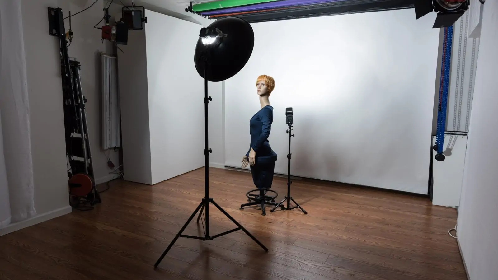Lola the manequin posing with beauty dish above her, aimed down, and speedlight behind her aimed at background