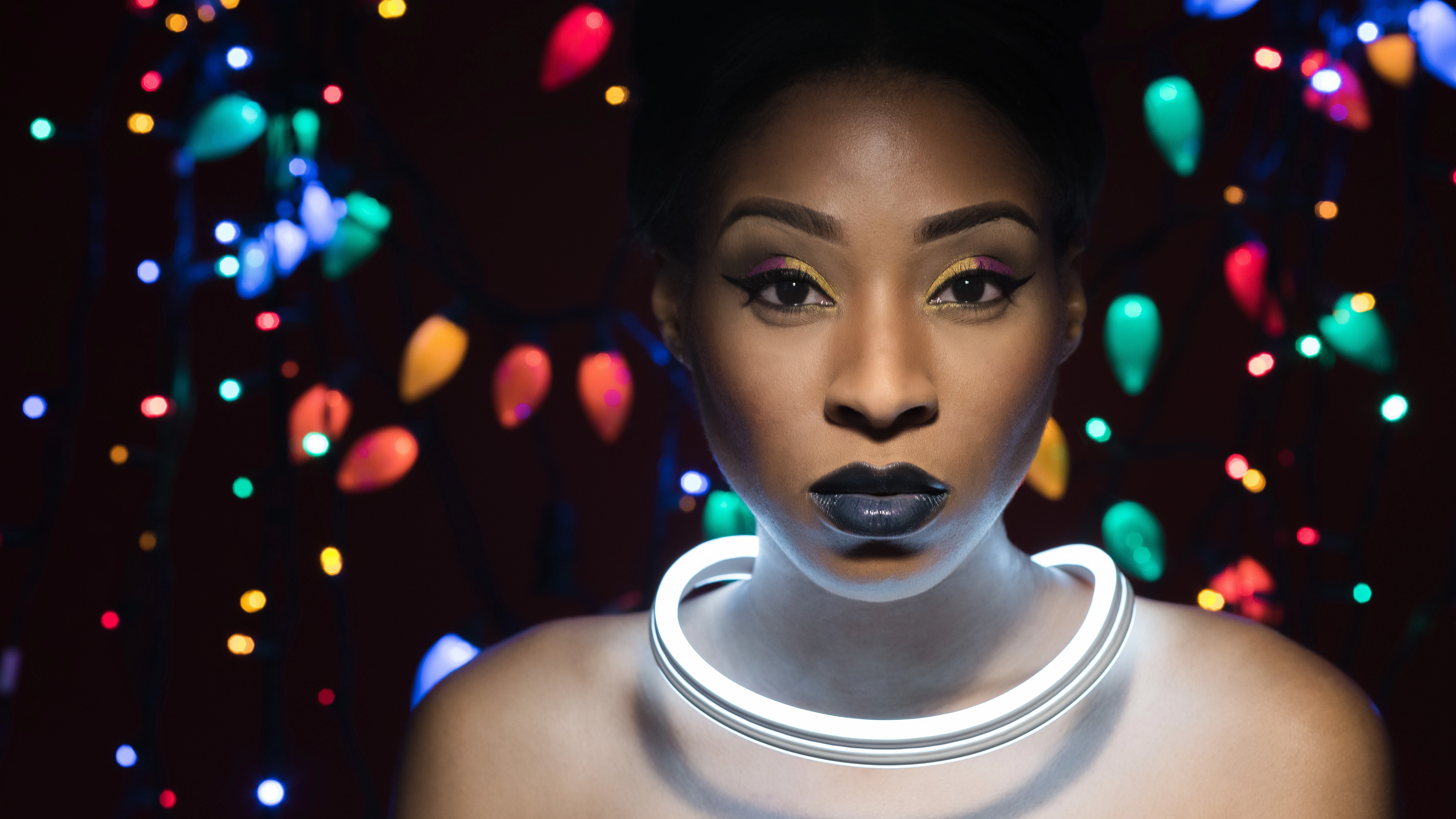 sixth of DIY Christmas Light portraits Monae with light on neck and Christmas lights in background on black
