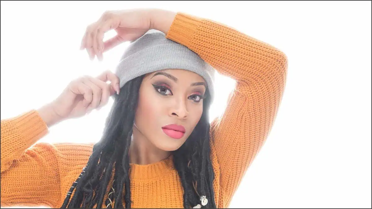 Person in an orange sweater adjusts their gray beanie, confidently posing with magmod-like charm against a bright white background.