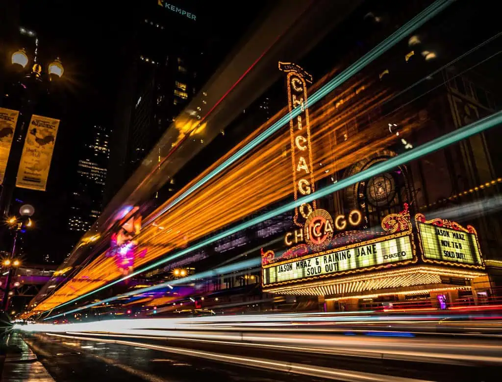 Bright light trails weave through the live composite of the illuminated Chicago Theater marquee at night, displaying "Jason Mraz & Raining Jane Sold Out.